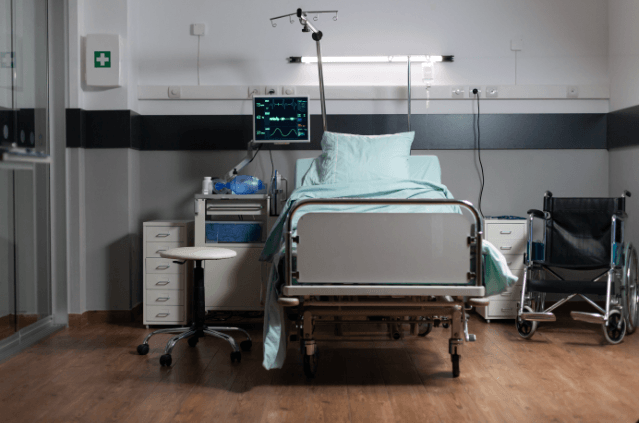 An empty hospital room with a bed, monitor and wheelchair.